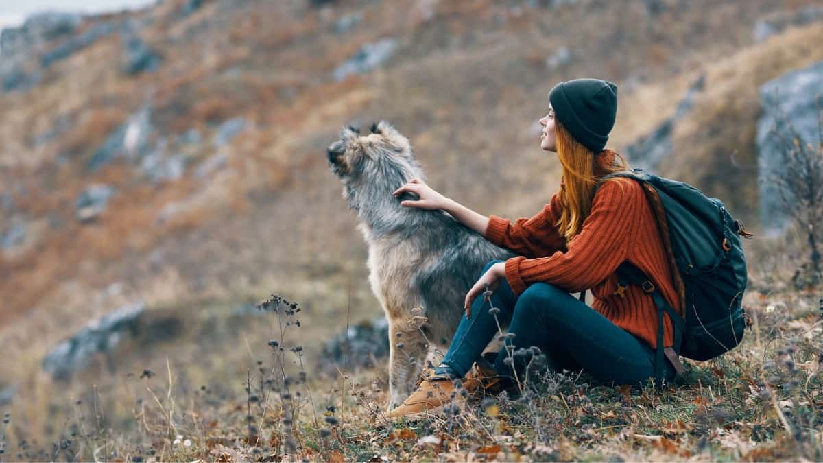 Woman sitting and backpacking with her dog on a hillside